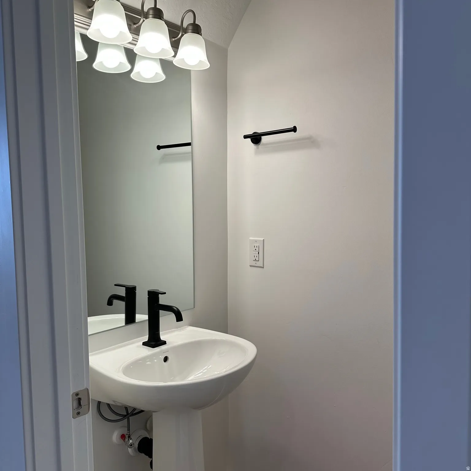 Pedestal sink with a matte black faucet, wall-mounted mirror, and vanity lighting with frosted glass shades