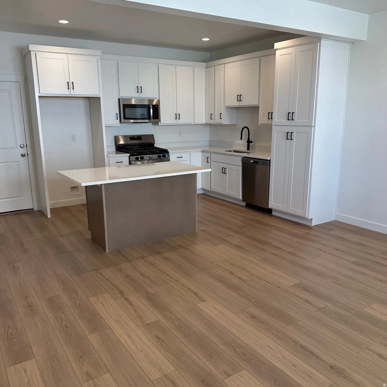 Bright kitchen with white cabinetry, stainless steel appliances, a center island with a light-toned countertop, and wood-finish flooring