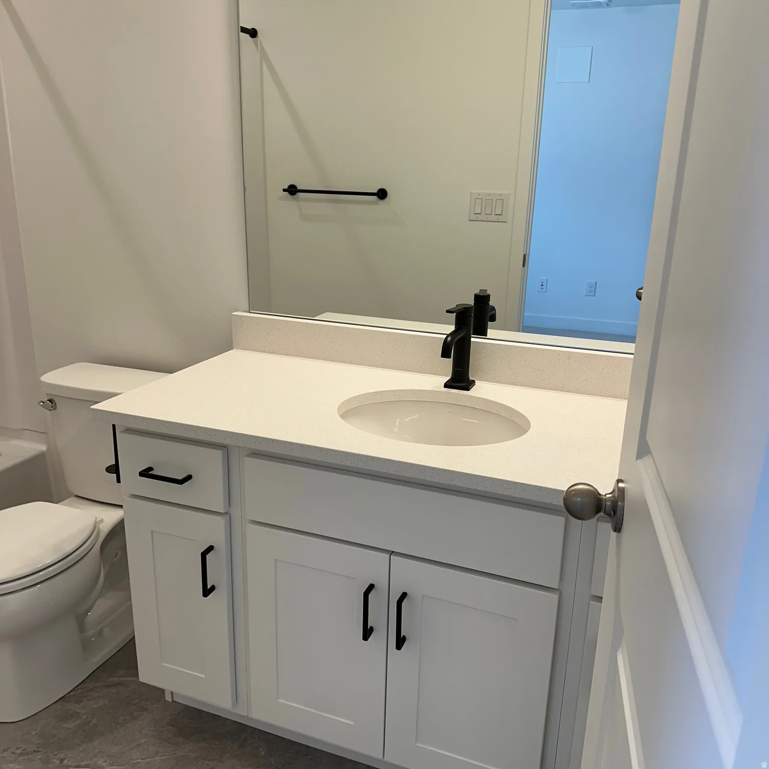 White vanity with a built-in sink, solid surface countertop, and matte black faucet