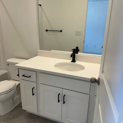White vanity with a built-in sink, solid surface countertop, and matte black faucet