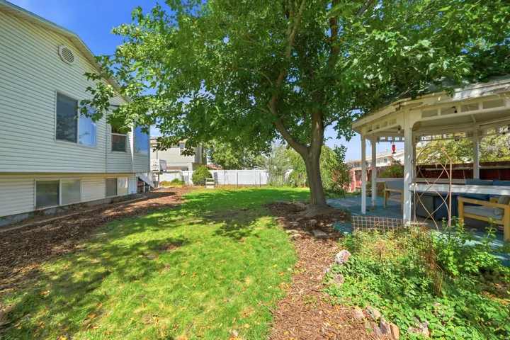 Expansive lawn with mature trees, a white vinyl fence, and a white gazebo