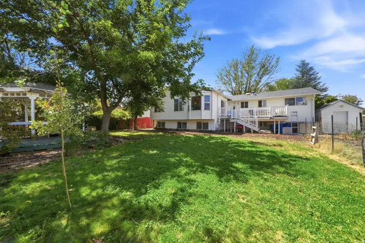 Expansive backyard featuring a manicured lawn, mature trees, a multi-level deck, and a detached storage shed
