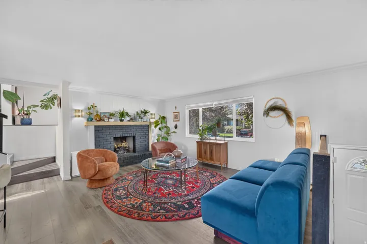 Living area featuring wood-finish flooring, a fireplace with a black brick surround and wood mantel, white paneled accent wall, and large windows