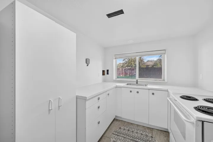 White cabinetry with minimalist hardware, white countertops, stainless steel sink with a single-handle faucet, and a window providing natural illumination
