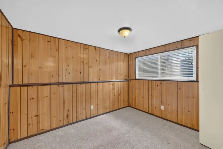 Carpeted flooring, wood paneling with horizontal trim, and a horizontal window with blinds