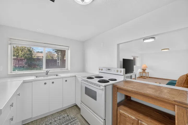 White cabinetry with silver hardware, white countertops, built-in dual basin sink, and a white electric range