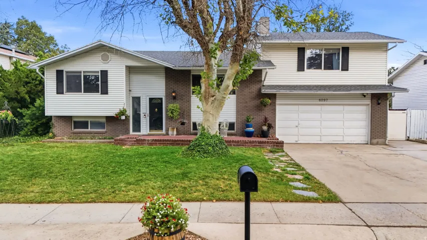 Split-level residence featuring a brick and siding exterior, two-car garage, front lawn, and mature tree