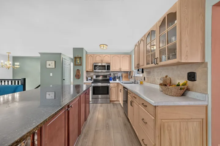 Kitchen featuring wood-finish flooring, stainless steel appliances, and wood cabinetry with glass-front upper units