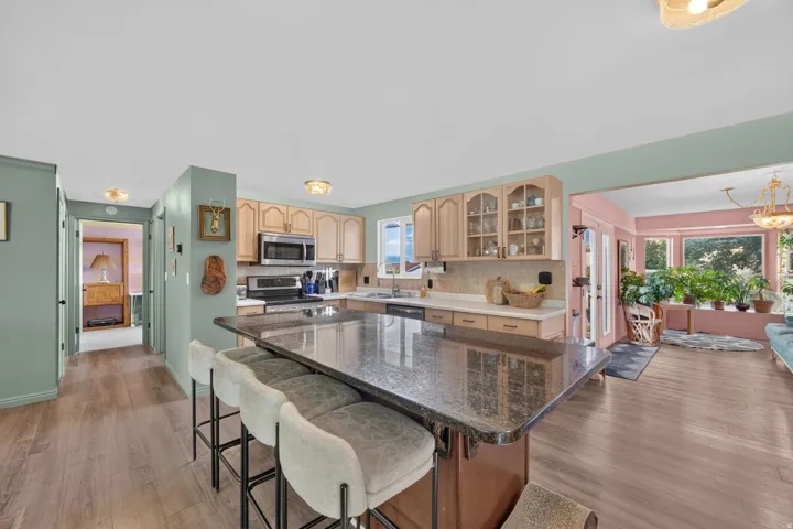 Wood-finish flooring, light wood cabinetry, stainless steel appliances, dark stone countertop, and bay windows