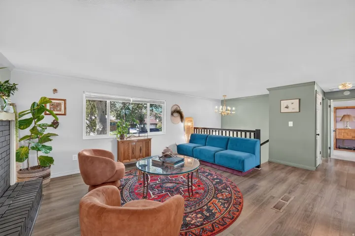 Wood-finish flooring throughout, framed window, fireplace with brick surround, built-in staircase railing, and ceiling-mounted chandelier