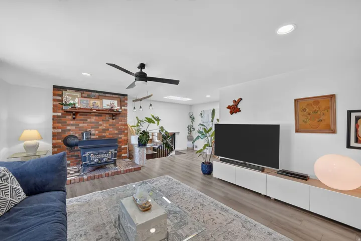 Living space featuring wood-finish flooring, a brick fireplace with a wood-burning stove, a ceiling fan, recessed lighting, and a built-in media console