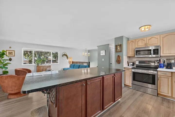 Kitchen island with a dark countertop and rich wood-finish cabinetry, stainless steel appliances, and wood-finish flooring