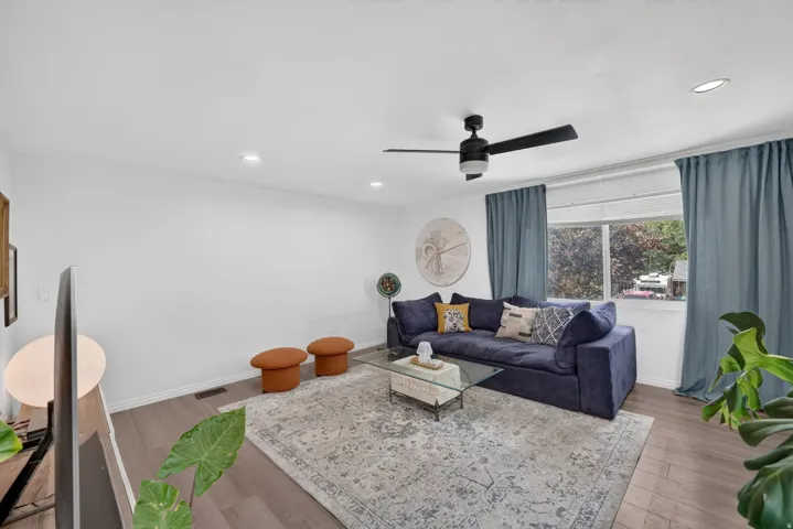 Recessed lighting illuminates the room, featuring wood-finish flooring and a ceiling fan