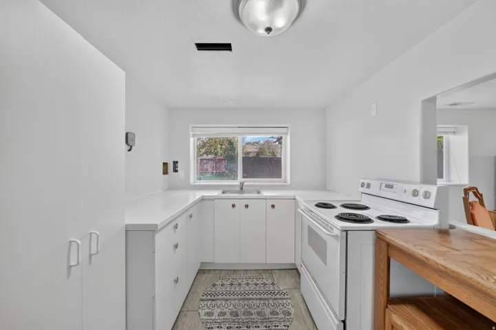 U-shaped kitchen with white cabinetry, white countertops, built-in range, and a window above the sink