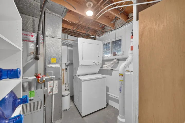 Stackable washer and dryer, exposed ceiling joists, utility sink, windows, and shelving