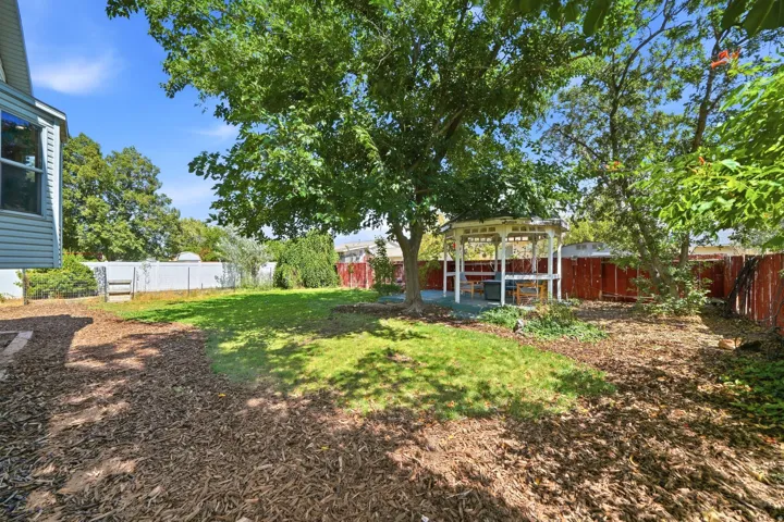 Expansive backyard featuring a manicured lawn, established trees, and a white gazebo