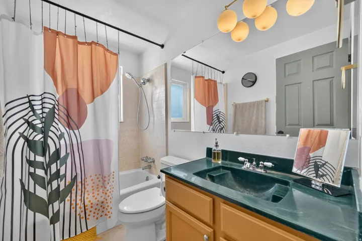 Built-in tub with tile surround, vanity with an integrated sink, wood-finish cabinetry, and overhead lighting fixture