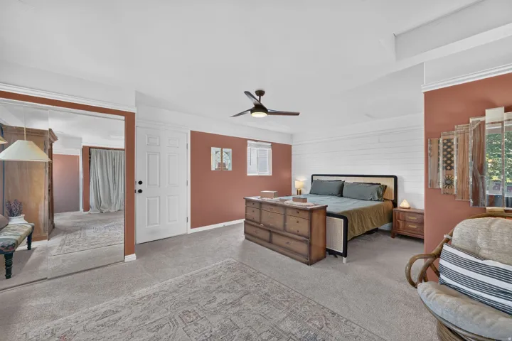 Wall-to-wall carpeting with an ornate area rug, white paneled accent wall, ceiling fan with integrated lighting, and a full-length mirrored wall