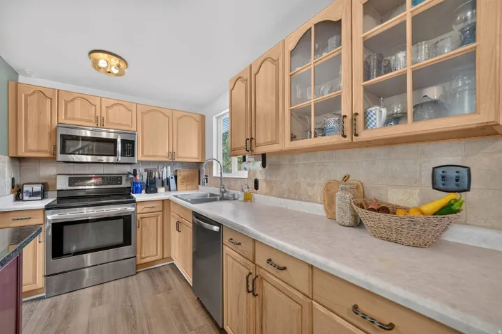 Wood-finish flooring with light-toned cabinetry, stainless steel appliances, and neutral tile backsplash