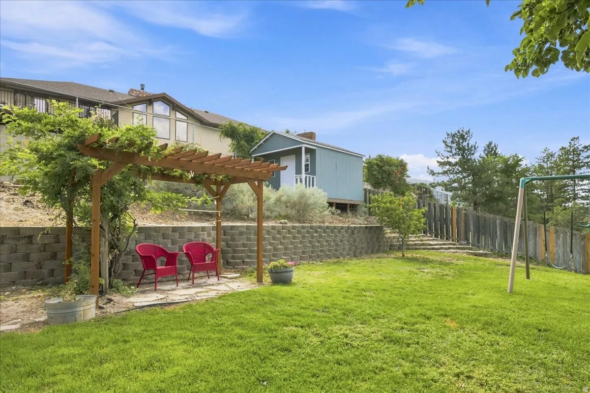 Expansive backyard featuring a lush lawn, a wooden pergola, a retaining wall, a detached shed, and mature trees