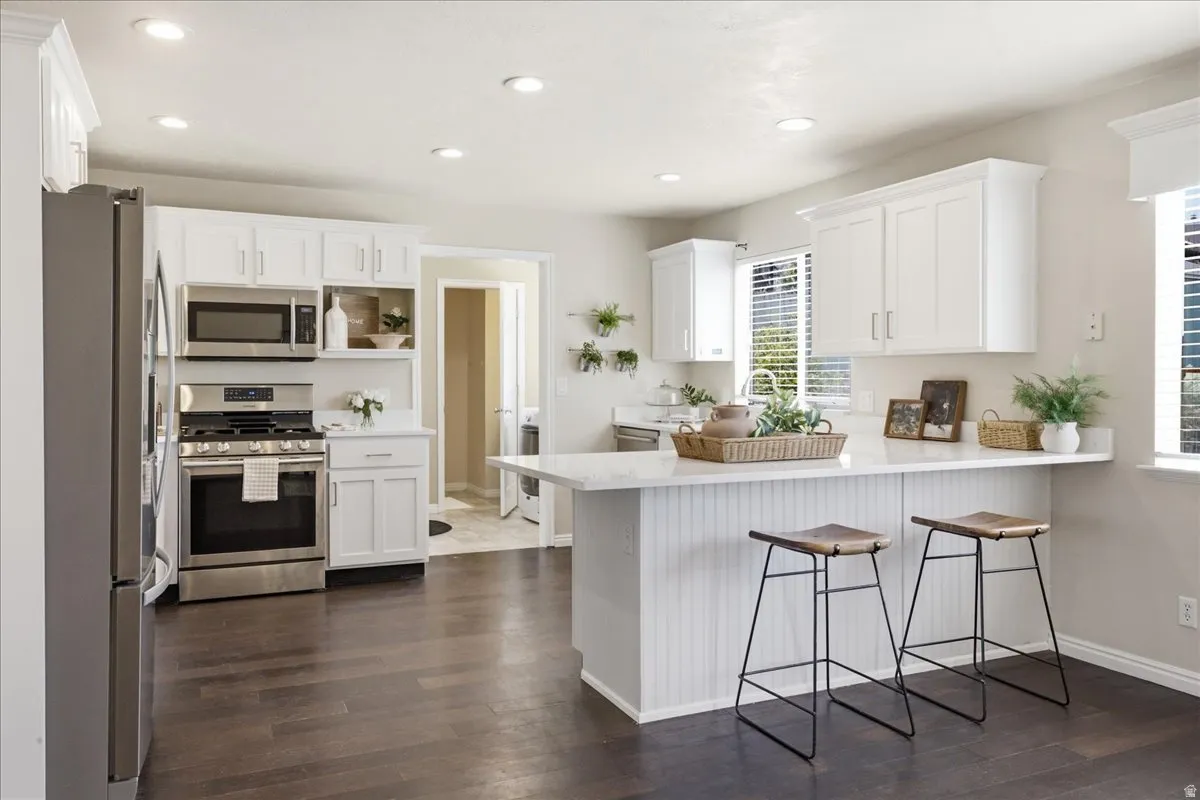 Kitchen featuring white shaker cabinetry, stainless steel appliances, dark wood-finish flooring, recessed lighting, and a kitchen island with seating