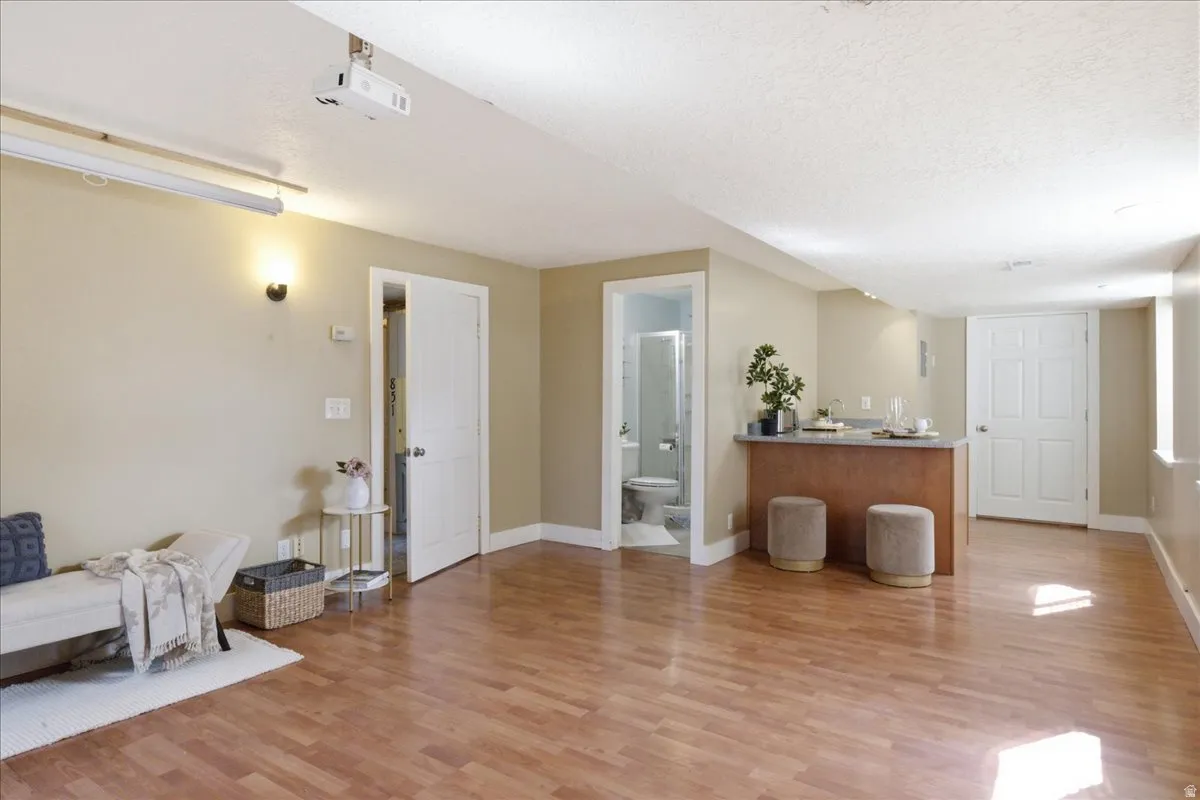 Spacious room with wood-finish flooring, a built-in wet bar, and a ceiling-mounted projector with a retractable screen