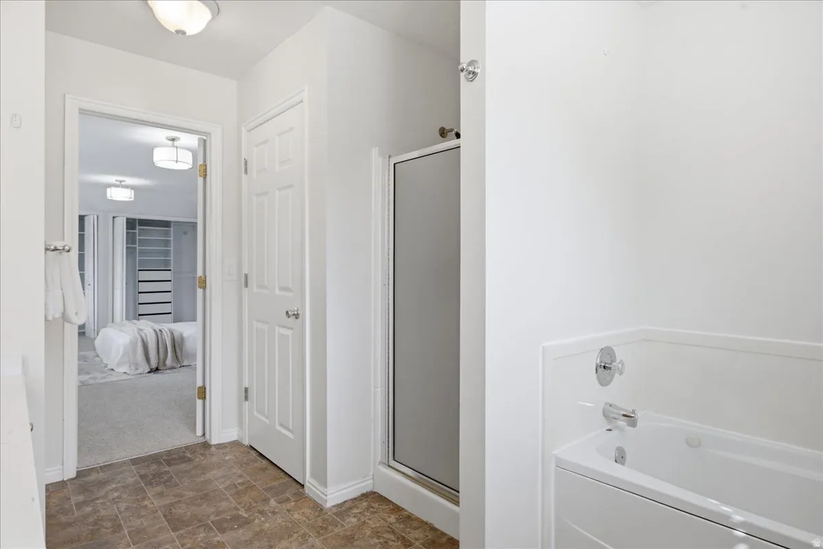 Brown-toned tile flooring, shower enclosure with frosted glass, and white built-in bathtub with chrome fixtures