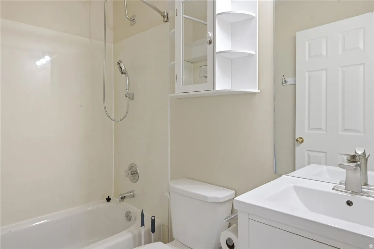 White vanity with an integrated sink and brushed nickel faucet, built-in medicine cabinet with open shelving, and a combination tub and shower with a handheld showerhead