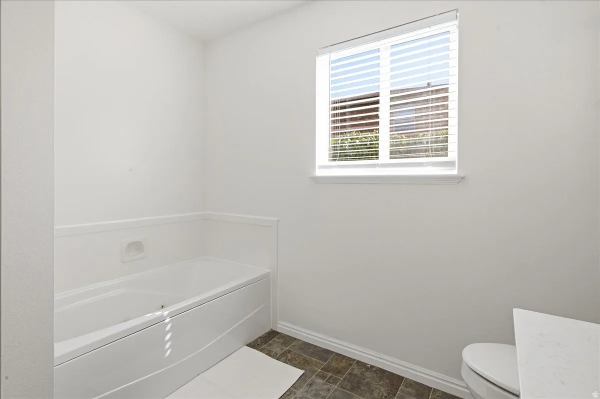 White bathtub with white wainscoting and a window with horizontal blinds