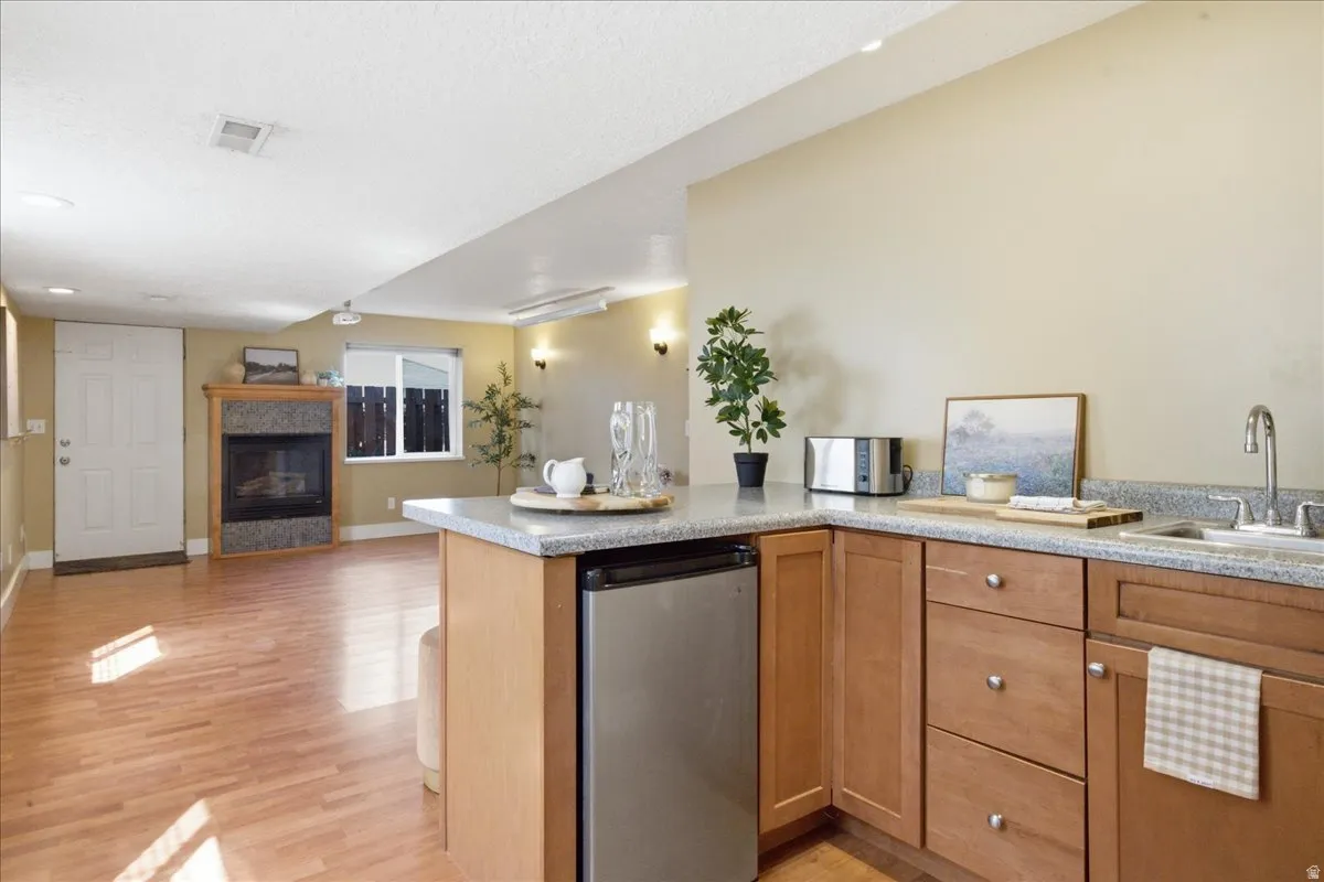 Kitchenette with wood-finish cabinetry, stainless steel sink, and light-toned countertops