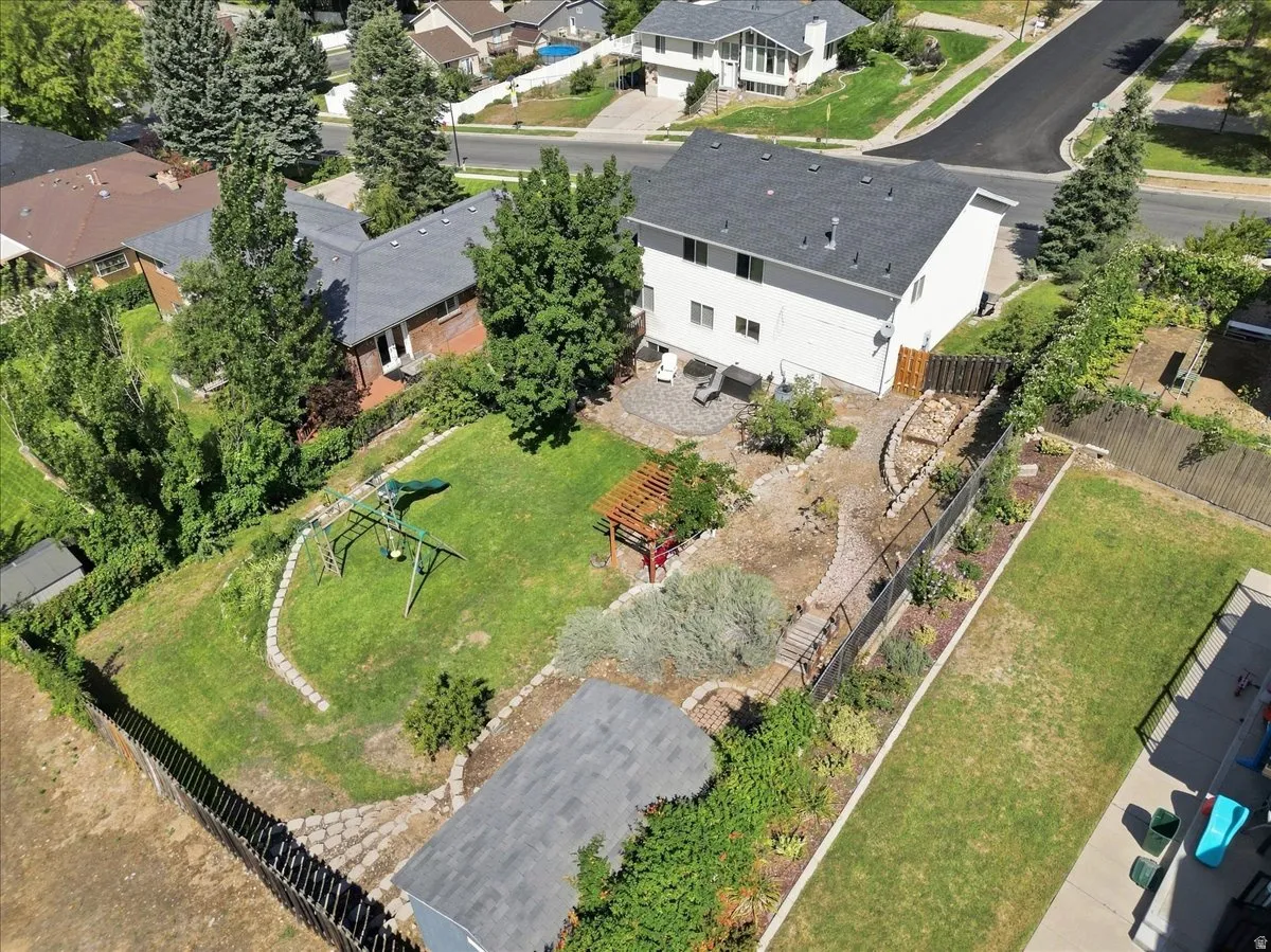 Expansive fenced backyard featuring a manicured lawn, established landscaping, a paved patio, and a storage shed