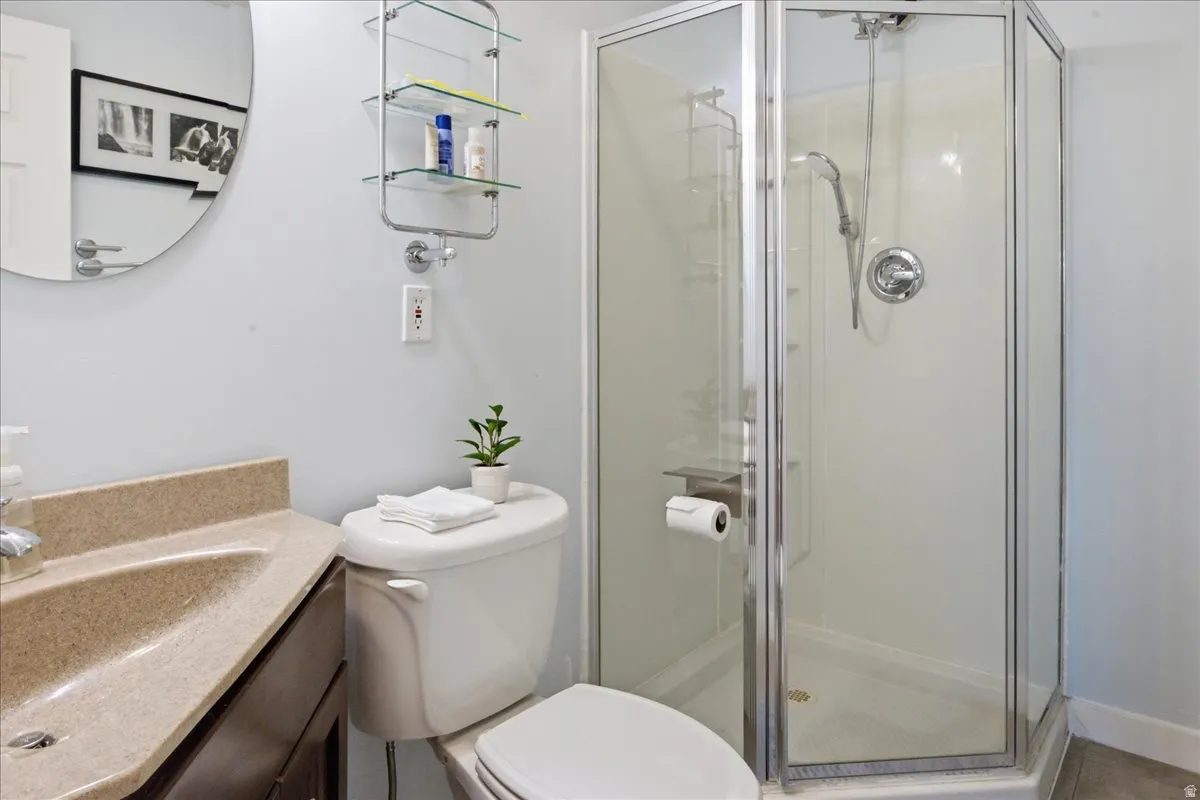 Corner glass-enclosed shower with a handheld showerhead, a single-basin vanity with a light-colored countertop, and a circular wall mirror