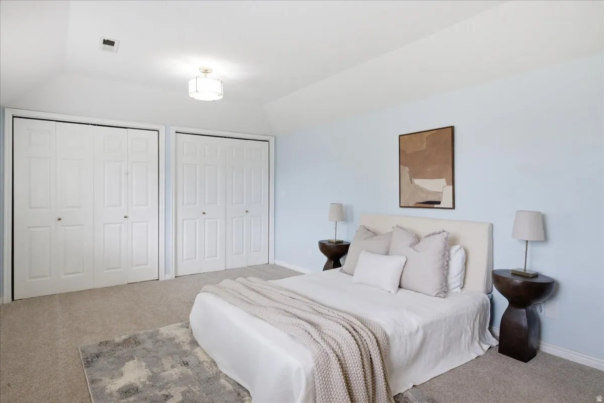 Vaulted ceiling, two bifold door closets, carpet flooring, and a flush mount light fixture