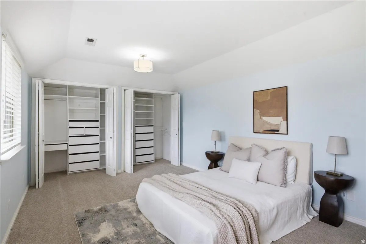 Vaulted ceiling with an attached light fixture, window with blinds, and built-in closet organization systems