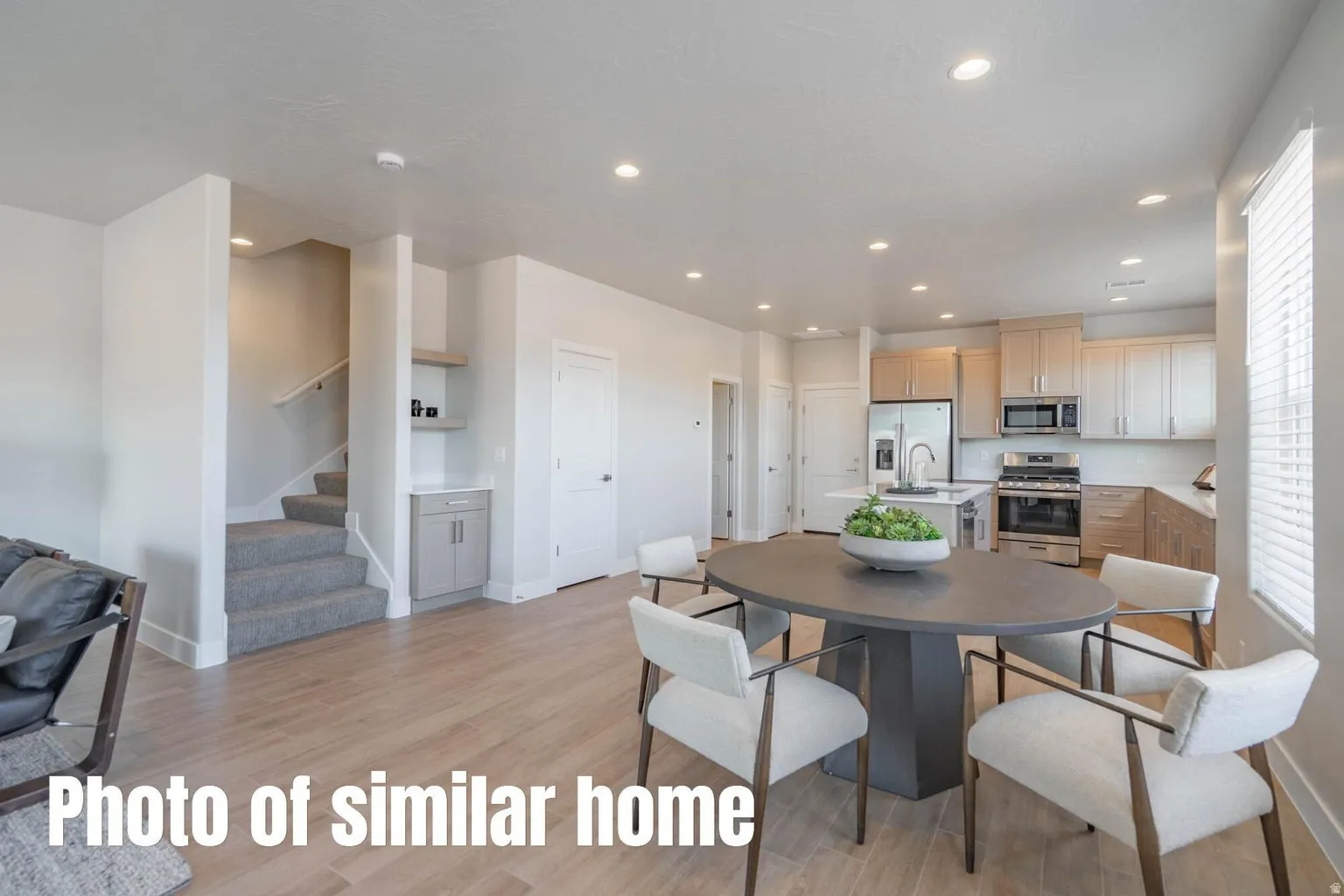 Open-concept main living area with wood-finish flooring, recessed lighting, and a kitchen featuring stainless steel appliances, light cabinetry, and an island with a sink