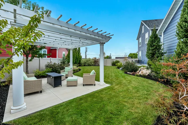 Expansive backyard featuring a pergola, concrete patio, lush green lawn, mature landscaping, and privacy fencing