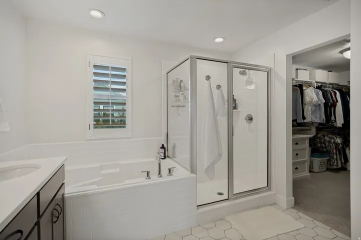 White hex tile flooring, recessed lighting, built-in soaking tub with white subway tile surround, glass-enclosed shower, and built-in closet organization system