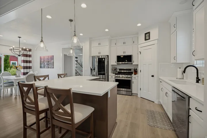 Kitchen featuring a U-shaped island with seating, white shaker-style cabinetry, stainless steel appliances, a white tile backsplash, and light wood-finish flooring