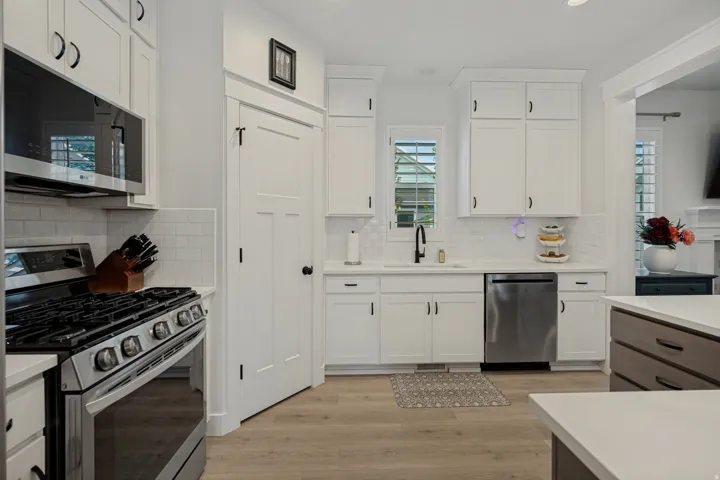 Modern kitchen featuring light wood-finish flooring, white cabinetry with dark hardware, stainless steel appliances, and a white subway tile backsplash