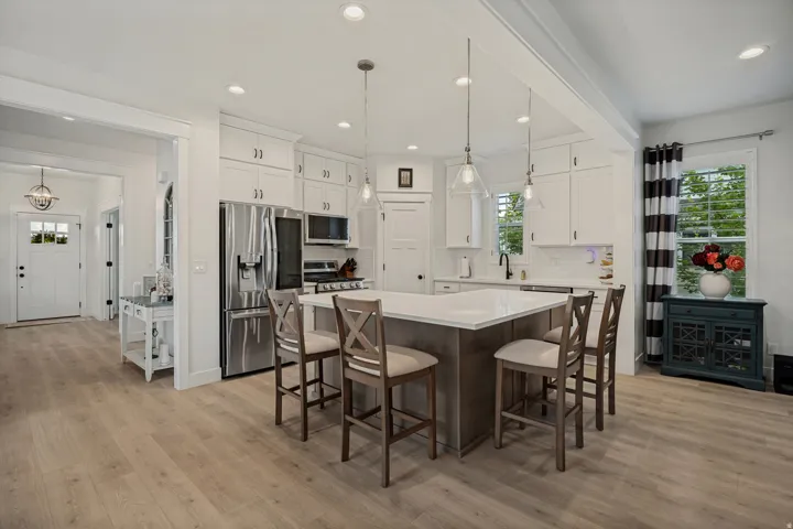 Open-concept kitchen featuring an island with seating, pendant lighting, stainless steel appliances, white cabinetry, and wood-finish flooring