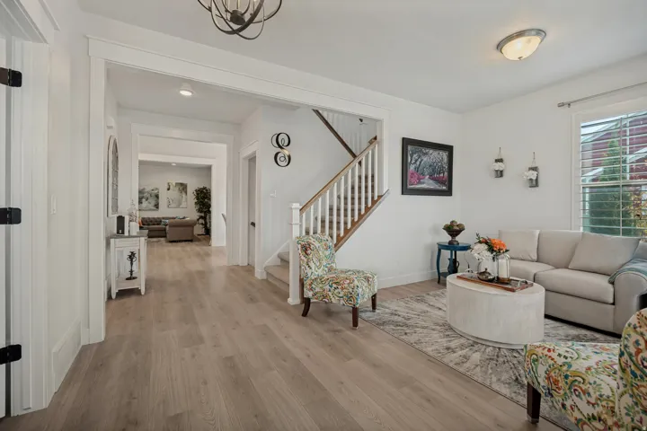 Light wood-finish flooring throughout, white painted trim and doors, staircase with white newel posts and wood handrail, recessed lighting, and an overhead decorative light fixture