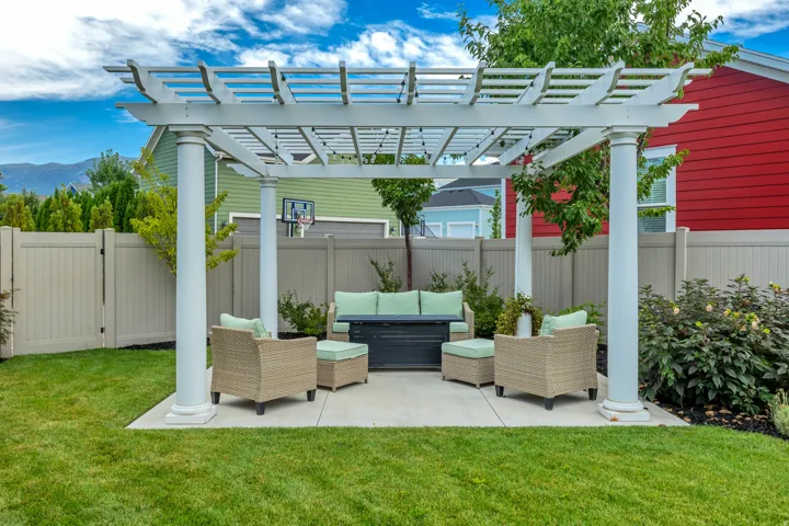Expansive backyard featuring a manicured lawn, a concrete patio, a white pergola, and a privacy fence