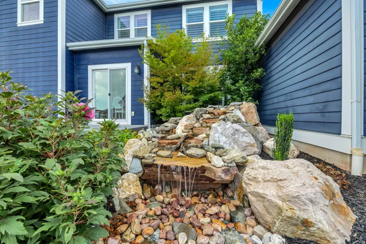 Landscaped exterior featuring a rock waterfall, mature shrubs, and a sliding glass door