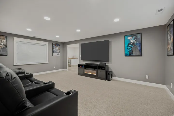 Recessed lighting, light-toned carpeting, built-in media console with integrated fireplace, and a window with blinds