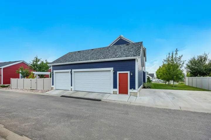Two-car garage with white doors, dark blue siding, a red entry door, gray shingle roofing, and a concrete driveway