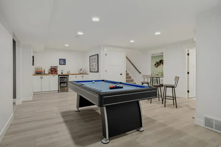 Spacious recreation room featuring wood-finish flooring, recessed lighting, and a built-in wet bar with white cabinetry, a wood countertop, and a beverage refrigerator