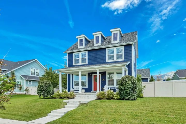 Two-story residence featuring dormer windows, a covered front porch with white pillars, and a red entry door