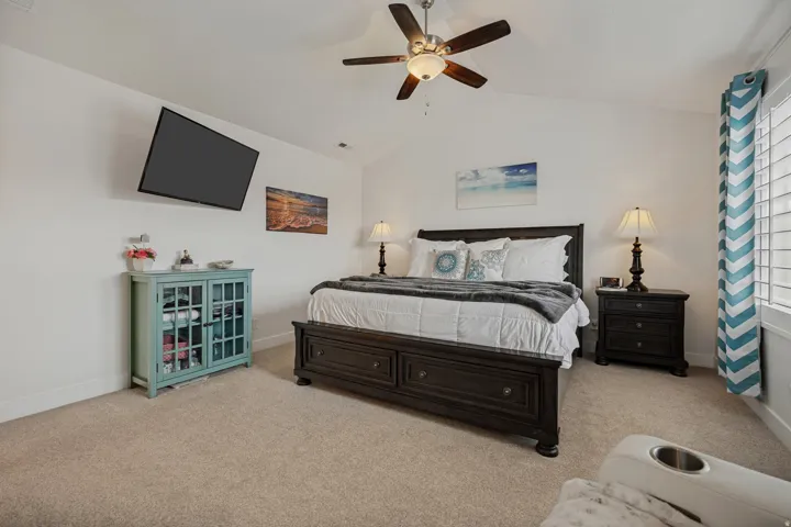 Vaulted ceiling with a ceiling fan, carpet flooring, a wall-mounted television, and window with plantation shutters