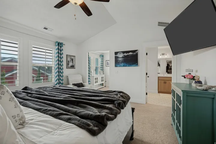 Vaulted ceiling with a ceiling fan, dual windows with plantation shutters, carpet flooring, and a vanity with a rectangular sink and wood-finish cabinetry