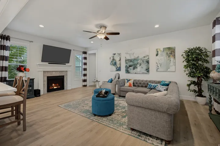 Spacious living area featuring light wood-finish flooring, a contemporary fireplace with a stone surround and mantle, and recessed lighting